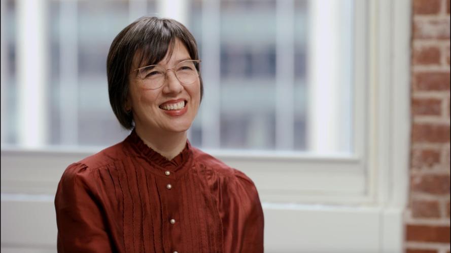 Karen Rommelfanger smiling in a warmly lit room. A window and brick wall are visible behind her.